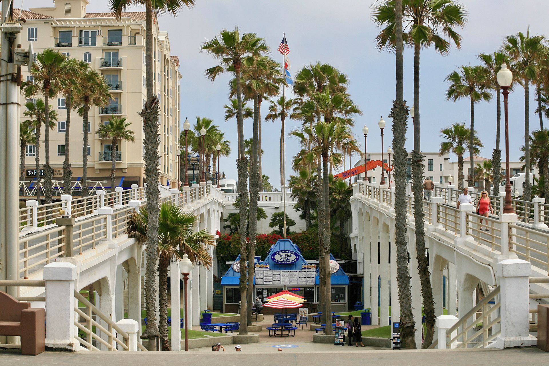 A coastal promenade with palm trees, a bridge, and a seafood restaurant.