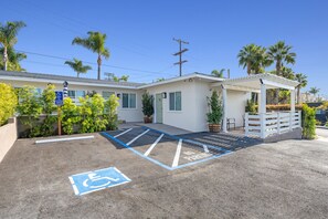 A parking area with a handicapped accessible space, a building with a green door, and a covered patio area with plants.