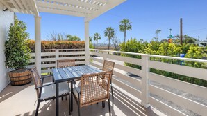 Eine überdachte Terrasse mit Tisch und Stühlen, umgeben von weißen Geländern und viel Grün.