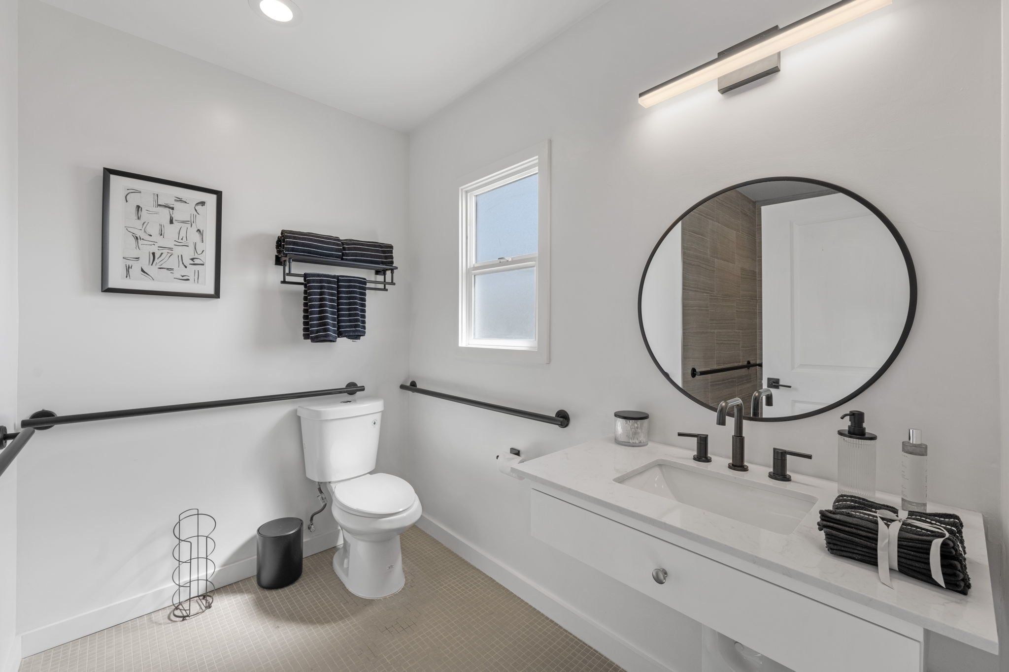 Un baño moderno con inodoro, lavamanos, espejo, toallero y ventana.