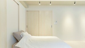 Un dormitorio minimalista con una cama individual, un armario de madera y una pared lisa.