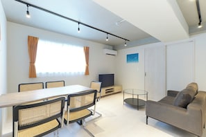 A modern living room with a dining area, a sofa, a TV, and a large window with curtains. - River Residence BOTAN by Tranova (Tokyo)