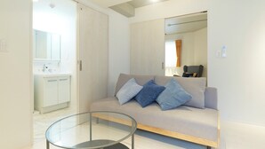 Una sala de estar moderna con un sofá, una mesita de centro de vidrio y un baño con lavamanos y espejo.