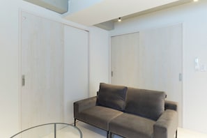 A modern room with a grey sofa, light wooden wardrobes, and a glass table. - River Residence BOTAN by Tranova (Tokyo)