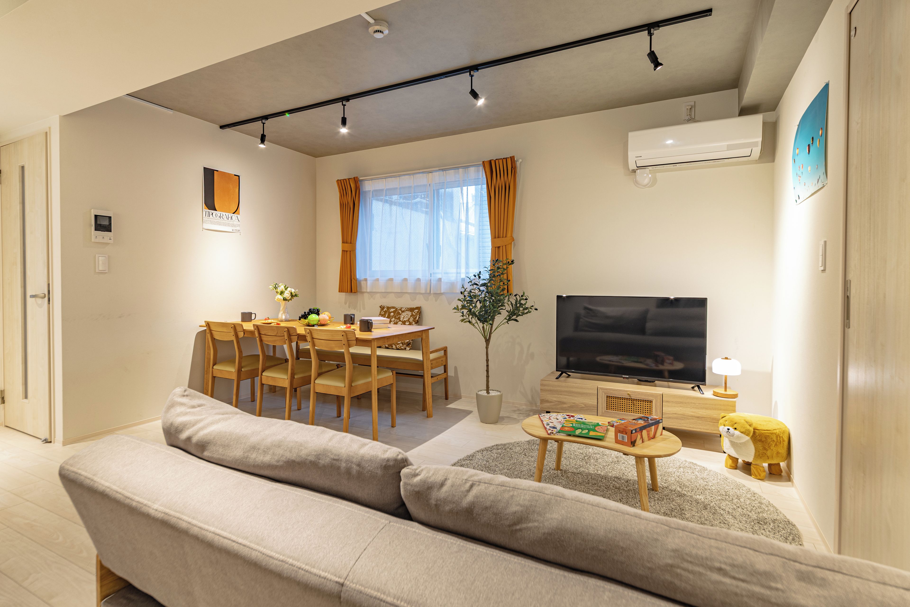 Ein modernes Wohnzimmer mit einer Couch, einem Esstisch, Stühlen, einem Fernseher und einem kleinen Tisch mit Büchern und einer Lampe.