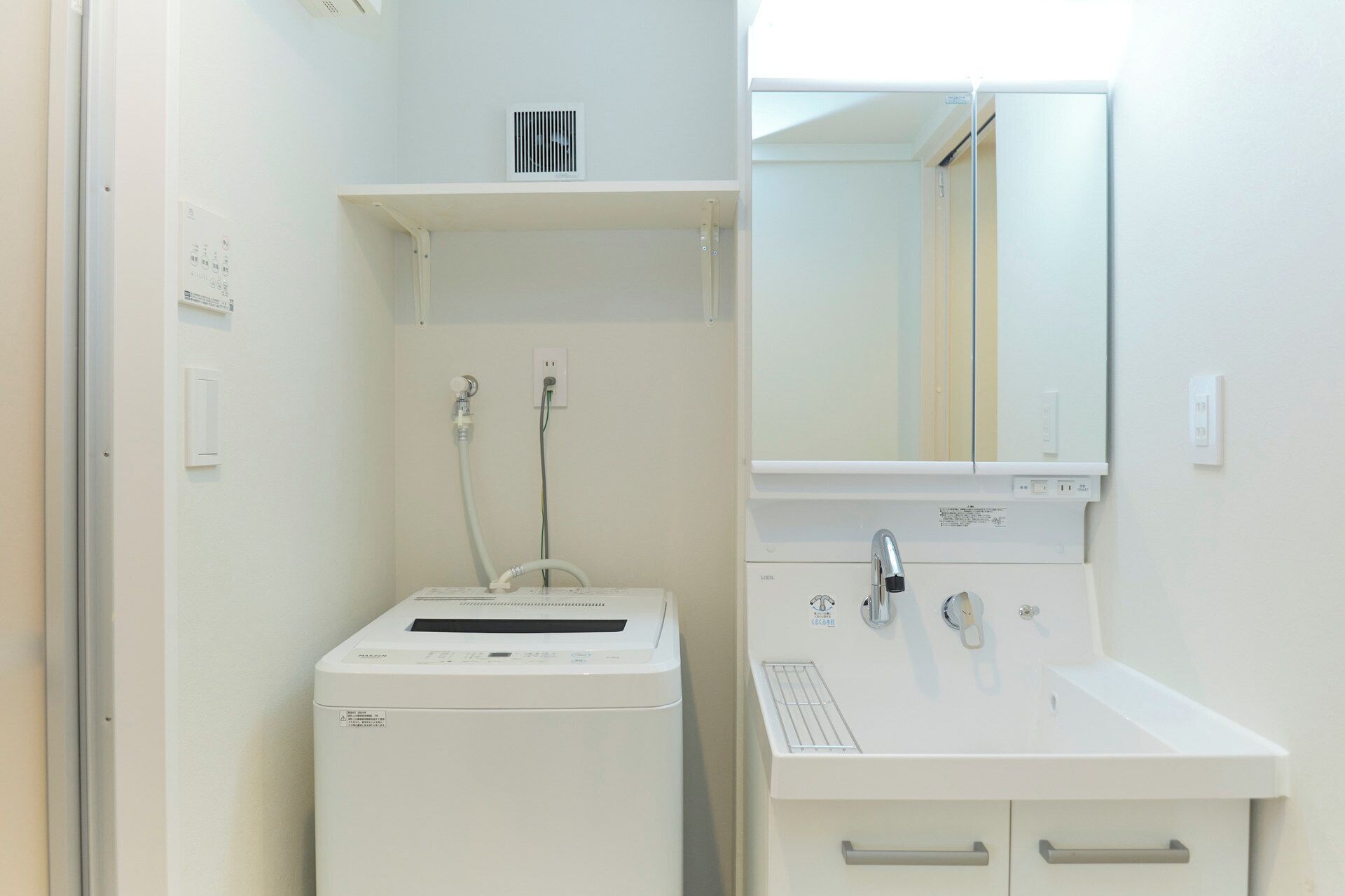 Une petite salle de bain équipée d’un lave-linge encastré, d’un lavabo avec un miroir et d’une petite étagère au-dessus du lave-linge.