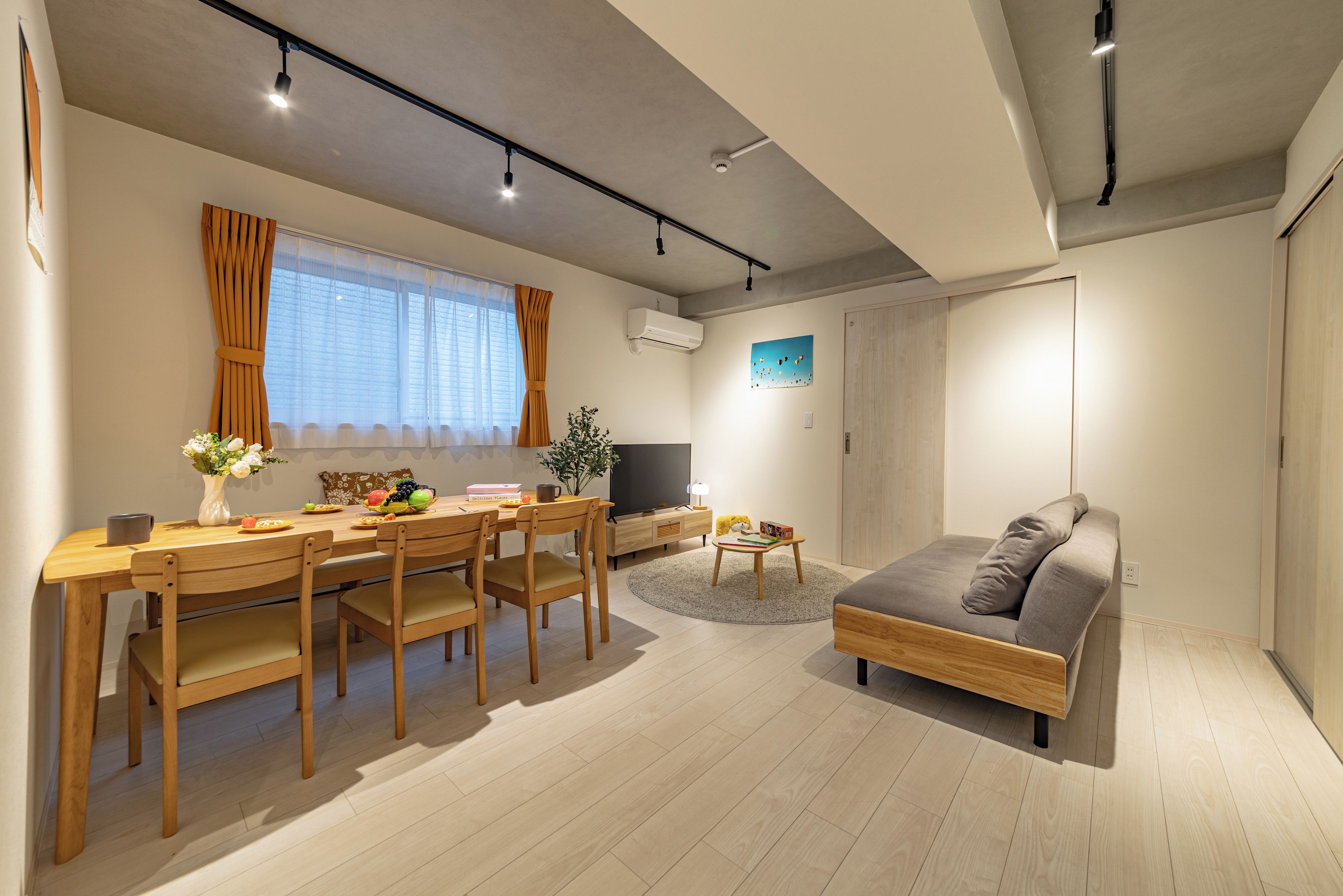 A modern living room with a wooden dining table, chairs, a sofa, a TV, and a small rug.