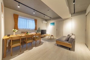 A modern living room with a wooden dining table, chairs, a sofa, a TV, and a small rug. - River Residence BOTAN by Tranova (Tokyo)