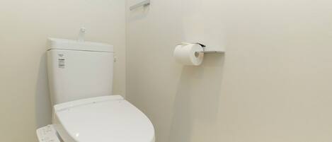 Inodoro blanco con panel de control, dispensador de papel higiénico en la pared y piso de mármol.