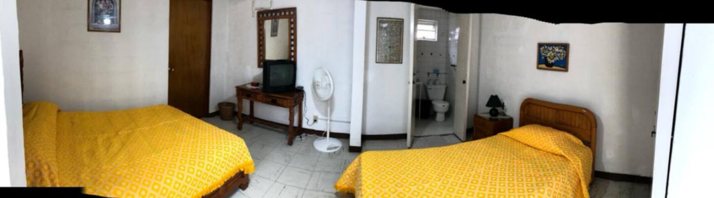 Ein Zimmer mit zwei Betten, einem Schreibtisch, einem Fernseher, einem Ventilator und einem durchgegangenen Tür sichtbaren Badezimmer.