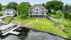 A large, two-story house with a covered dock and a landscaped garden. - Downtown Lakefront Home on Lake Chetek with hot tub & pontoon rental (Chetek)