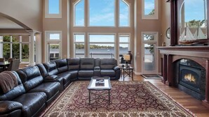 A spacious living room with a large L-shaped black leather sofa, a patterned rug, and a fireplace. - Downtown Lakefront Home on Lake Chetek with hot tub & pontoon rental (Chetek)