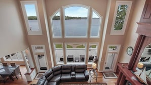 A spacious living room with a large sectional sofa, a fireplace, and multiple windows offering views of a lake. - Downtown Lakefront Home on Lake Chetek with hot tub & pontoon rental (Chetek)