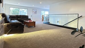 A modern living room with a leather sofa, a wooden coffee table, and a glass railing. - GeoHaven Rotorua — The Earth’s Embrace (Rotorua)