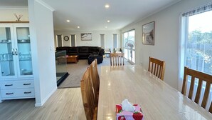 A spacious living area with a dining table, a black leather sofa, and a large window offering a view of the outdoors. - GeoHaven Rotorua — The Earth’s Embrace (Rotorua)