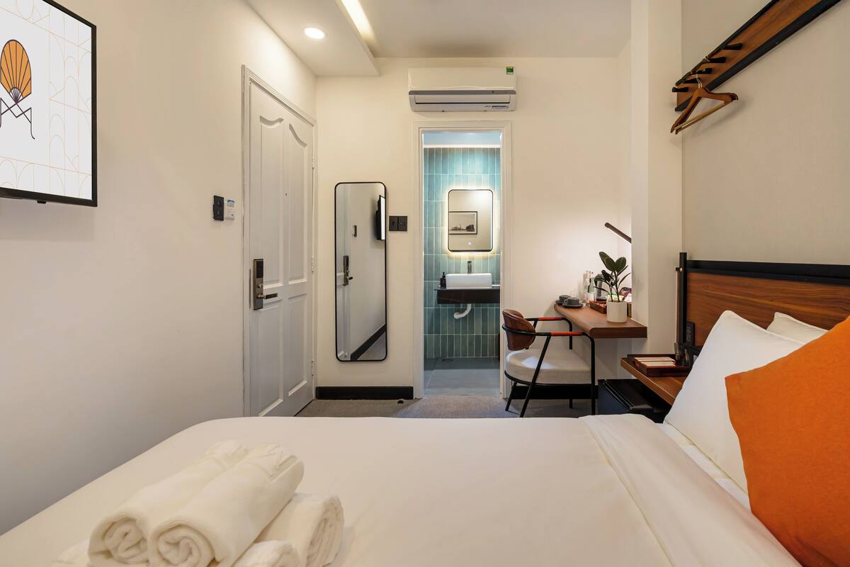 A hotel room with a bed, a desk, a chair, a mirror, and a bathroom visible through an open door.