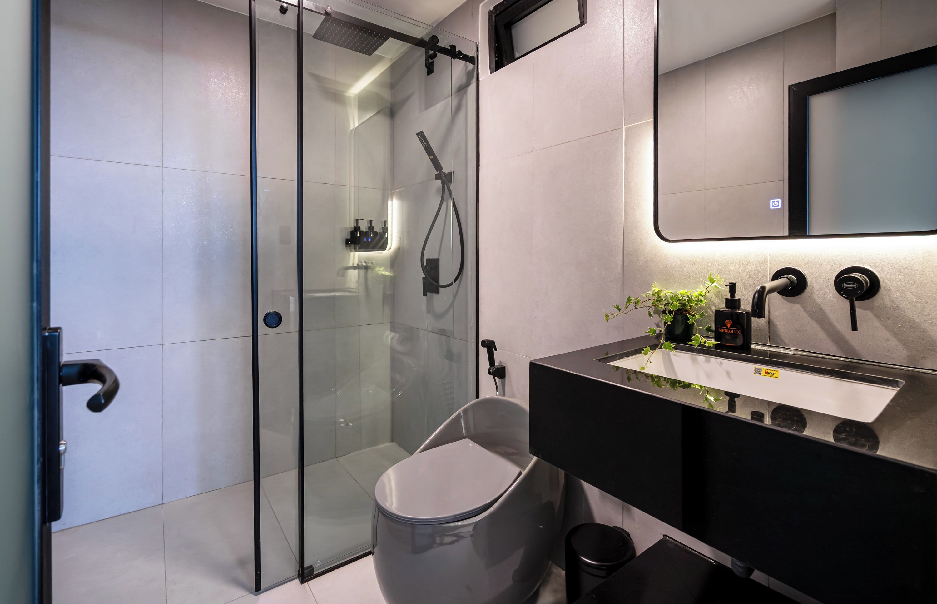 A modern bathroom with a glass-enclosed shower, a black sink with a mirror, and a small trash bin.