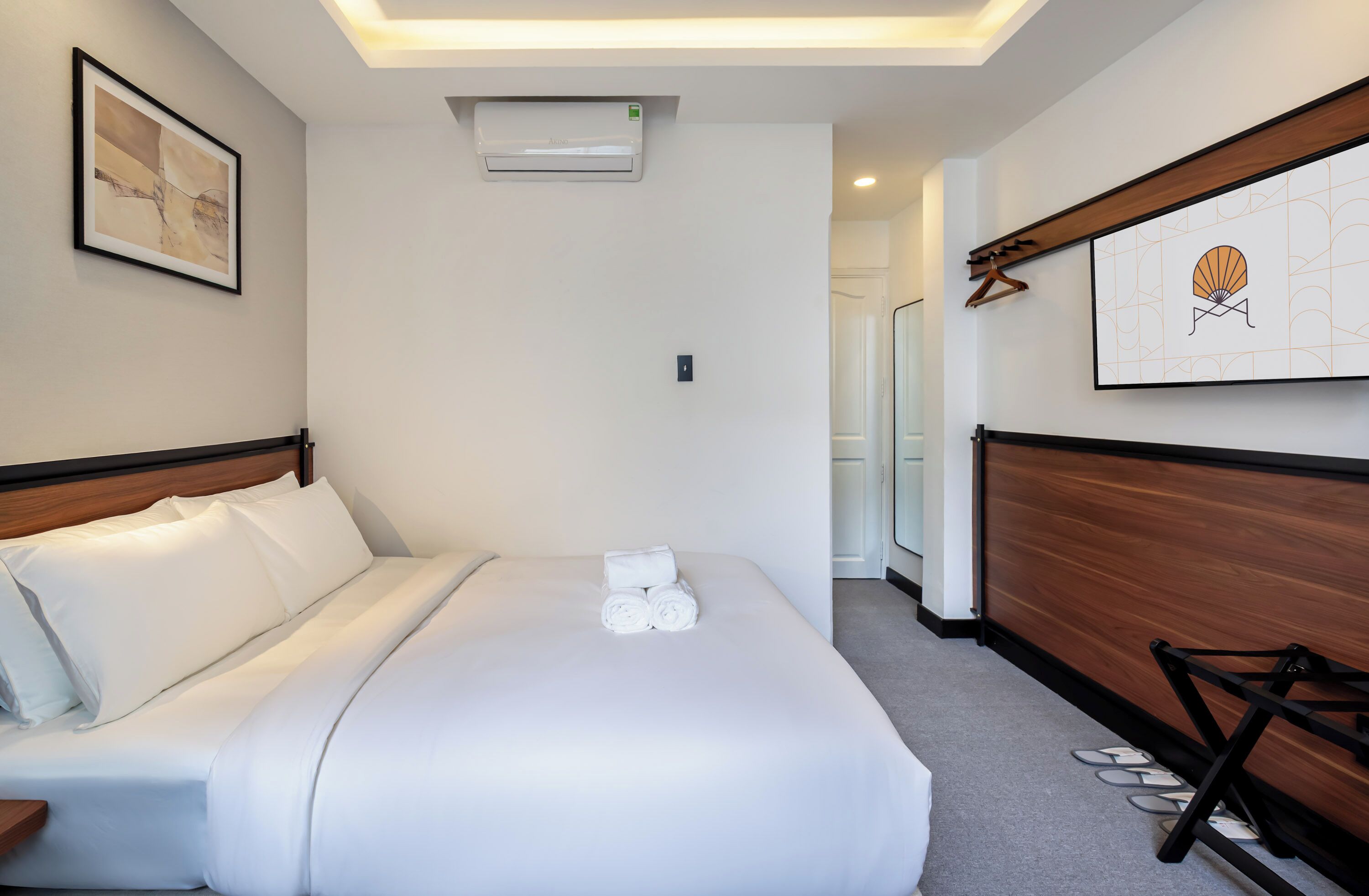 Habitación de hotel con una cama bien hecha, aire acondicionado de pared, un cuadro abstracto enmarcado y un panel de madera con un diseño decorativo.