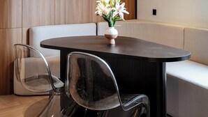 A modern dining area with a dark wooden table, clear chairs, a vase of white flowers, a wall-mounted air conditioner, and a decorative red wall piece. - Metrolux City Contemporary Hotel (Ho Chi Minh City)