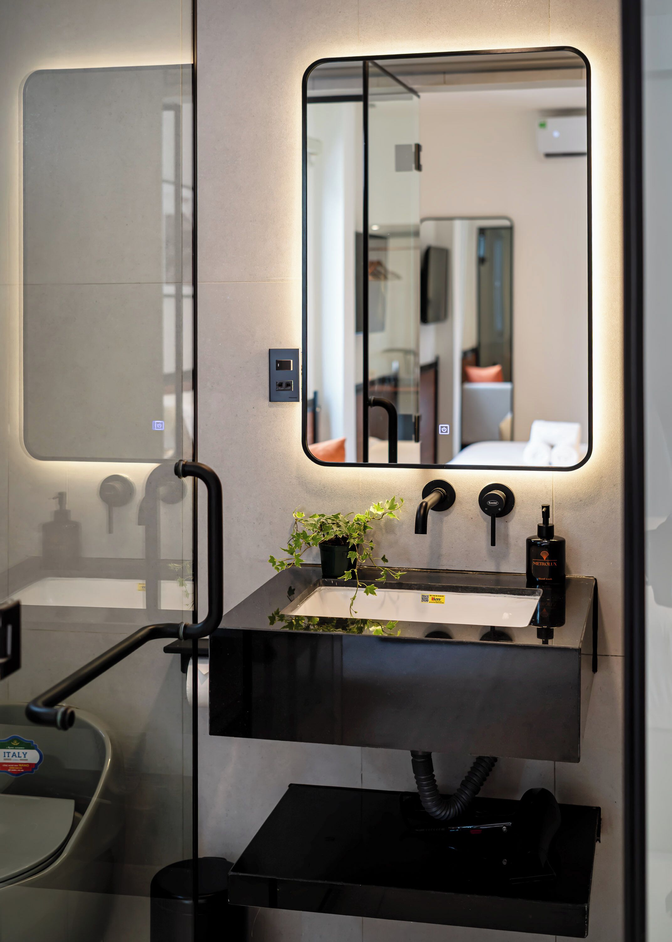 A modern bathroom with a black sink, a mirror, and a potted plant.