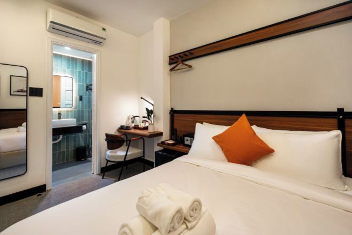 Quarto de hotel com uma cama, escrivaninha, cadeira, espelho e ar condicionado.