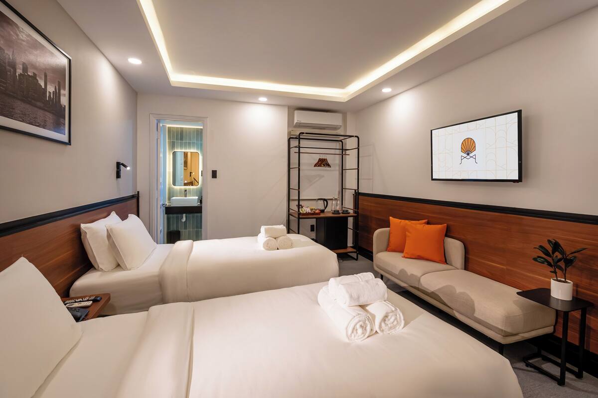 A hotel room with two beds, a sofa, a small table, a mirror, and a framed picture on the wall.