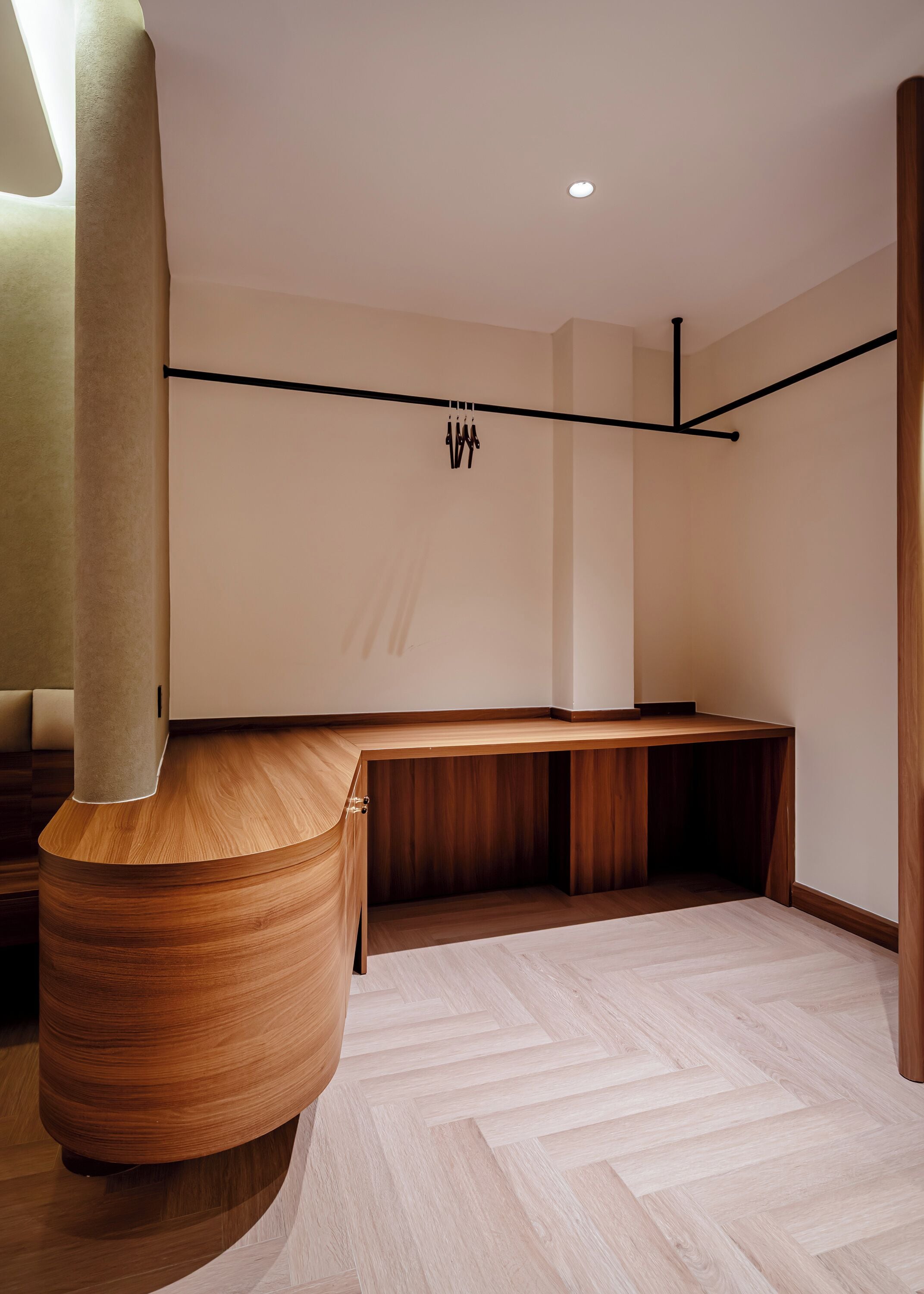 A modern, minimalist room with a curved wooden bench, a large cylindrical column, and a herringbone-patterned floor.