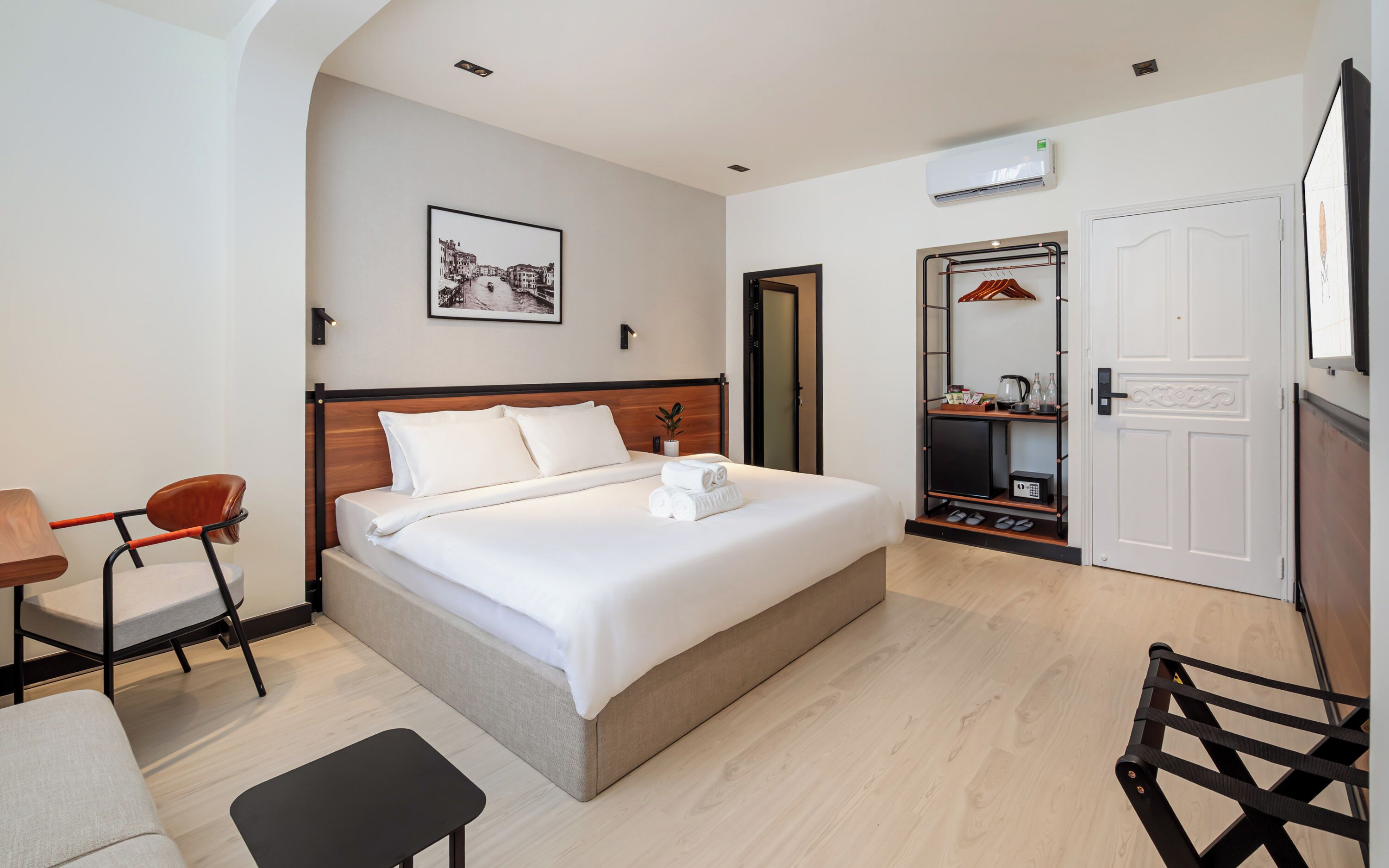 Une chambre d’hôtel avec un lit, un bureau, une chaise, une armoire et un tableau au mur.