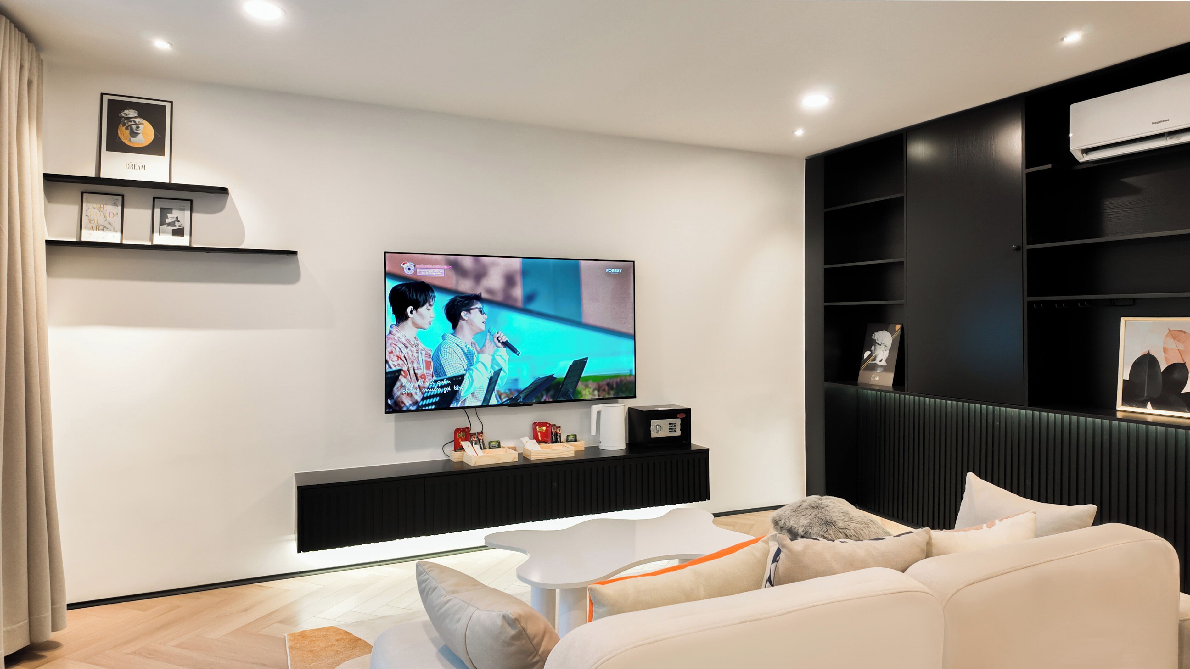 A modern living room with a flat-screen TV mounted on the wall, a white sofa, a coffee table, and a black entertainment unit with shelves.