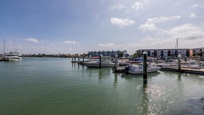 A marina with several boats docked, a large yacht, and a building with a distinctive arched window design in the background. - Completely renovated a one-bedroom, one-bathroom condo at Anglers Cove. (Marco Island)