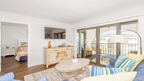 A modern living room with a sofa, a round wooden coffee table, a TV mounted on the wall, and a balcony with a glass door. - Completely renovated a one-bedroom, one-bathroom condo at Anglers Cove. (Marco Island)