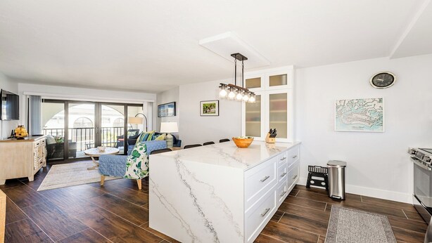 A modern kitchen with a marble island, wooden flooring, and a dining area with a blue sofa and a lamp. - Completely renovated a one-bedroom, one-bathroom condo at Anglers Cove. (Marco Island)