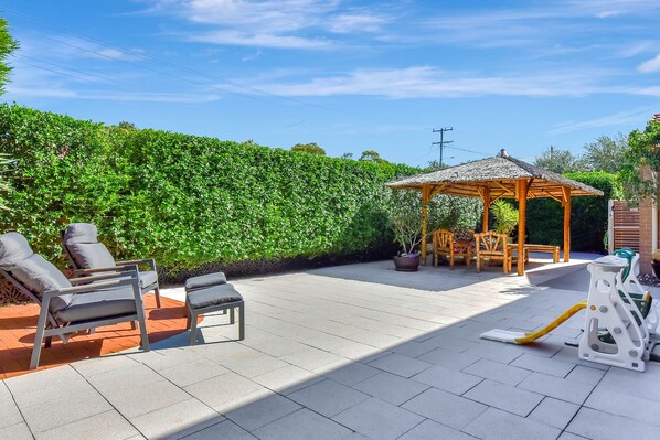 A patio with outdoor furniture, a gazebo, and a neatly trimmed hedge.