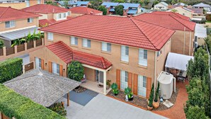 A residential building with a red-tiled roof, a covered patio area, and a water tank. - Nelly's Nest pet-friendly villa in Nelson Bay (Nelson Bay)