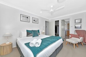 A modern bedroom with a bed, a chair, a desk, and a ceiling fan.