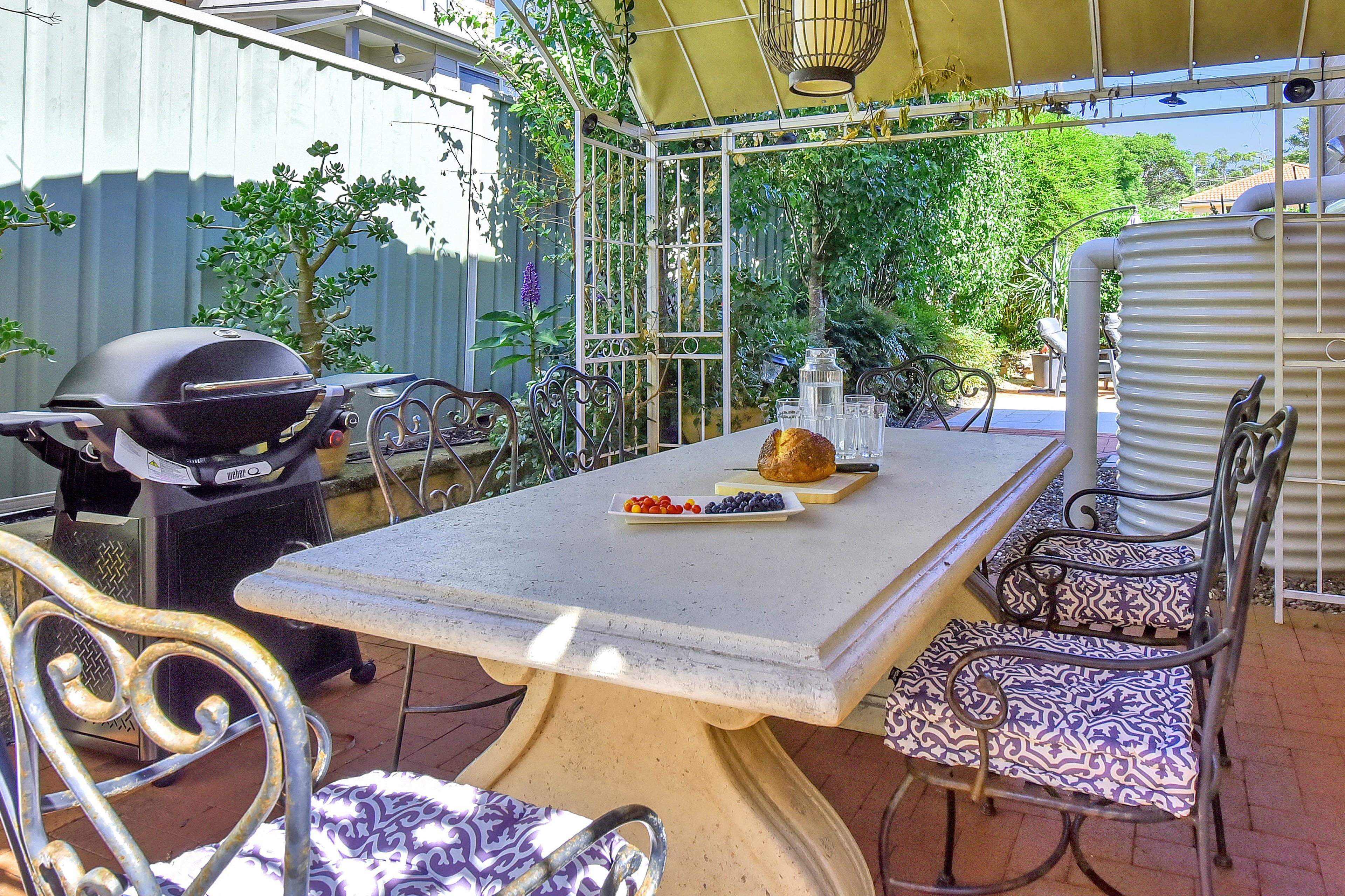 An outdoor patio with a grill, table, chairs, and a variety of plants.