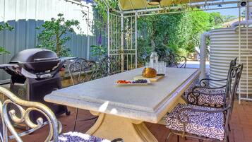 An outdoor patio with a grill, table, chairs, and a variety of plants.