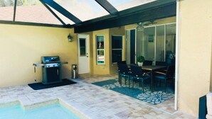 A covered patio with a barbecue grill, a pool, and a dining area with chairs and a table. - Charming 3-bedroom house with AC, WiFi in beautiful Naples (Naples)