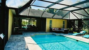 A swimming pool with a glass enclosure, a yellow wall, and a seating area with a couch and lounge chairs. - Charming 3-bedroom house with AC, WiFi in beautiful Naples (Naples)