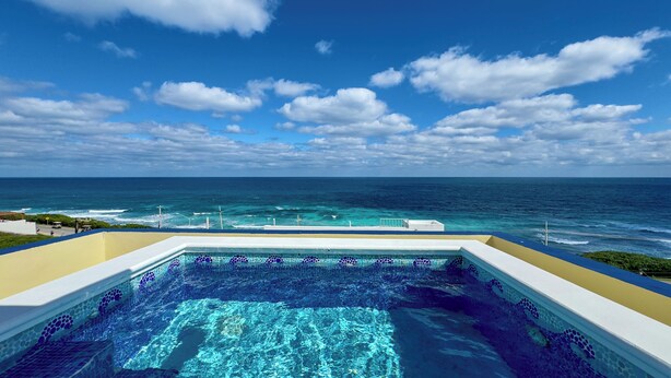 A pool with a mosaic design, overlooking a beach and the ocean.