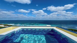 A pool with a mosaic design, overlooking a beach and the ocean.