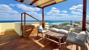 A wooden deck with outdoor furniture, a wooden staircase, and a view of the ocean and cityscape.
