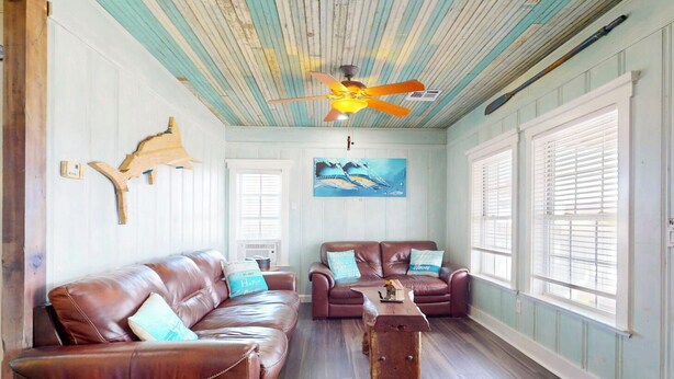 A room with a wooden ceiling, two leather sofas, a wooden coffee table, and a painting on the wall. - Charming Townhouse,  Shared pool, Great Location (Port Aransas)