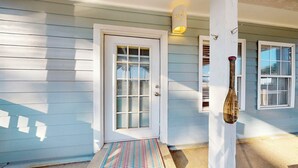 A house with a front door, a porch with a striped mat, and a wall-mounted light fixture. - Charming Townhouse,  Shared pool, Great Location (Port Aransas)
