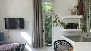 A modern kitchen with a flat-screen TV, a dining area with chairs, a sofa, and a patterned ottoman. - Treetop Bungalows (Siem Reap)