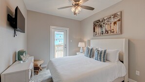 A bedroom with a bed, a ceiling fan, a television, a door leading to a balcony, and a painting on the wall. - Private Heated Pool, Golf Cart Included, Short Walk to the Beach (Port Aransas)