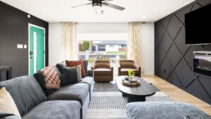 Ein modernes Wohnzimmer mit grauem Sofa, zwei Sesseln, einem Couchtisch und einem Deckenventilator.