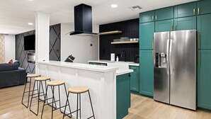 Eine moderne Küche mit einer zentralen Kochinsel, Barhocker, einem großen Kühlschrank und Türkis-Schränken.
