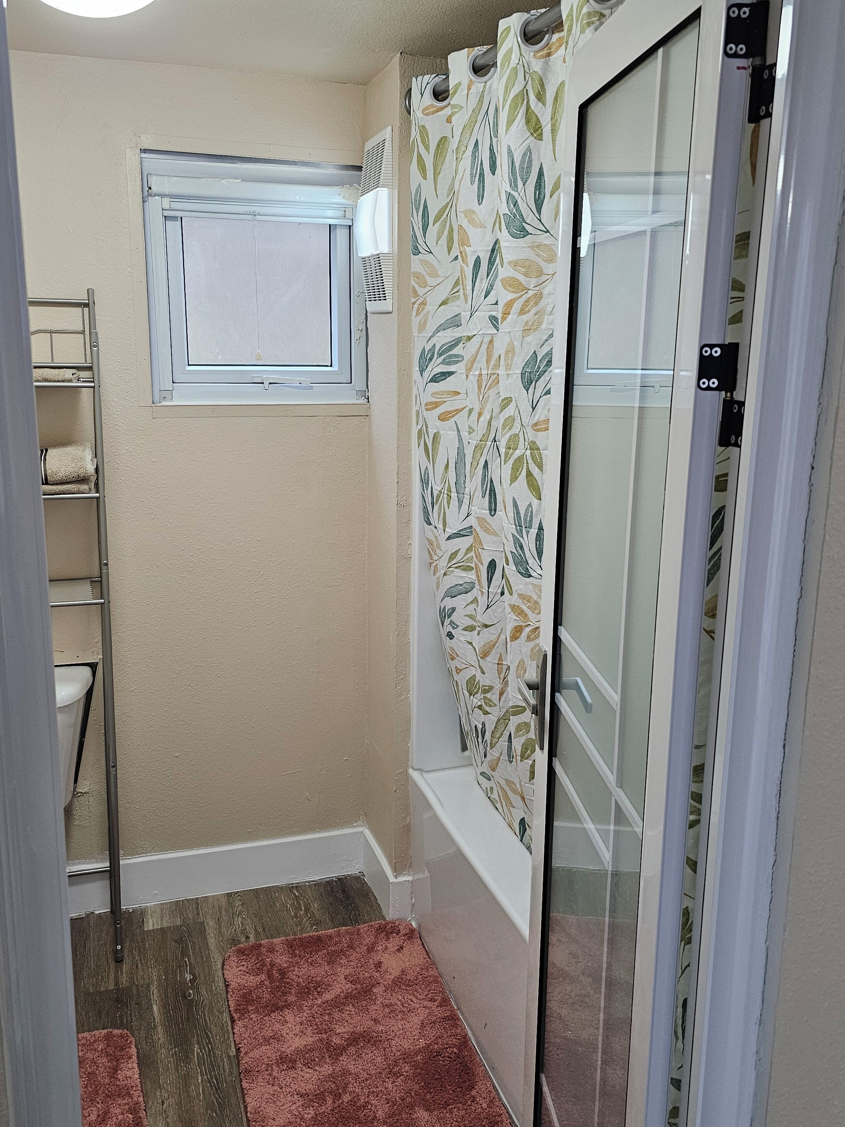 A bathroom with a shower, a towel rack, and a window.