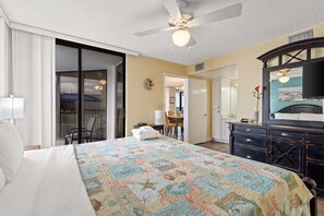 A hotel room with a large bed, a ceiling fan, a dark wooden dresser, and a view of the outside.
